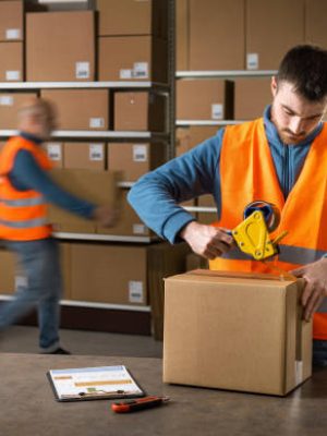 Warehouse worker sealing a delivery box using a tape dispenser gun, shipment and logistics concept